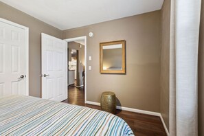 Een hotelkamer met een bed, een deur, een spiegel en een gang die naar een keuken leidt.