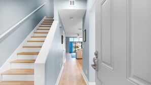 A staircase with wooden steps leading to a landing, a door with a silver handle, and a hallway with light blue walls and wooden flooring. - Beachwalk Villas 5079- On the Rocks (Miramar Beach)