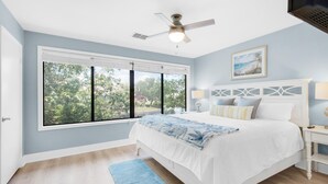 A bedroom with a large window, a bed, a ceiling fan, and a nightstand. - Beachwalk Villas 5079- On the Rocks (Miramar Beach)