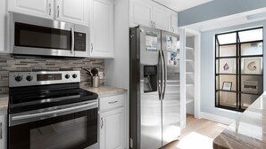 A modern kitchen with white cabinets, stainless steel appliances, and a tiled backsplash. - Beachwalk Villas 5079- On the Rocks (Miramar Beach)
