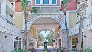 The entrance to The Village of Baytowne Wharf with a central archway, palm trees, and a brick pathway. - Beachwalk Villas 5079- On the Rocks (Miramar Beach)