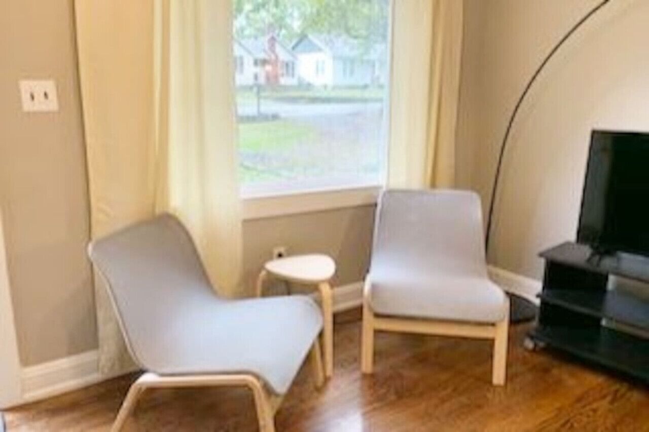 A room with two light grey chairs, a small round table, and a TV on a stand.