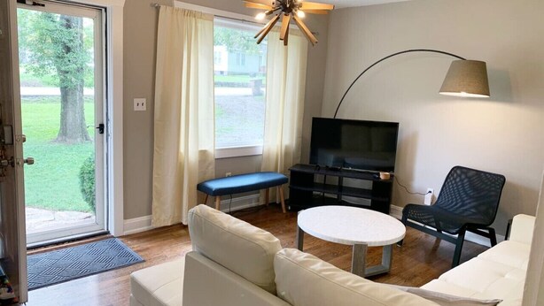 A living room with a sofa, a bench, a TV, a lamp, and a view of a garden through a sliding door. - Hangout House play, work, and visit (Nashville)