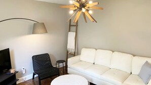 A modern living room with a white sofa, a black chair, a round coffee table, a TV, and a unique ceiling light fixture. - Hangout House play, work, and visit (Nashville)