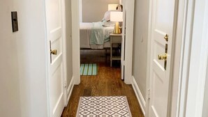 A narrow hallway leading to a bedroom with a bed, bedside lamp, and a small table. - Hangout House play, work, and visit (Nashville)