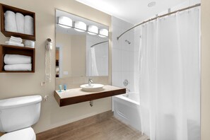 A modern bathroom with a toilet, a sink with a mirror above it, a shower with a curtain, and shelves with towels. - Bahia 4417- The Bahia Beach House (Miramar Beach)