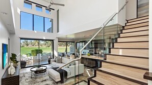 Ein modernes Interieur mit Treppe, einem Wohnbereich mit Sofa und Couchtisch sowie Blick ins Freie.