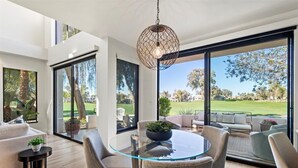 Ein modernes Wohnzimmer mit Glastisch, bequemen Sitzgelegenheiten und großen Fenstern mit Blick auf einen Golfplatz.