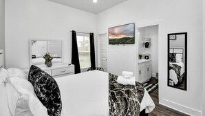 A modern bedroom with a bed, a mirror, a TV, and a window with curtains. - NEW,Vibrant, 4BR house, centrally located, photo wall, Gated  (Houston)