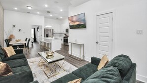 A modern living room with a green sofa, a coffee table, and a dining area with a white table and chairs. - NEW,Vibrant, 4BR house, centrally located, photo wall, Gated  (Houston)