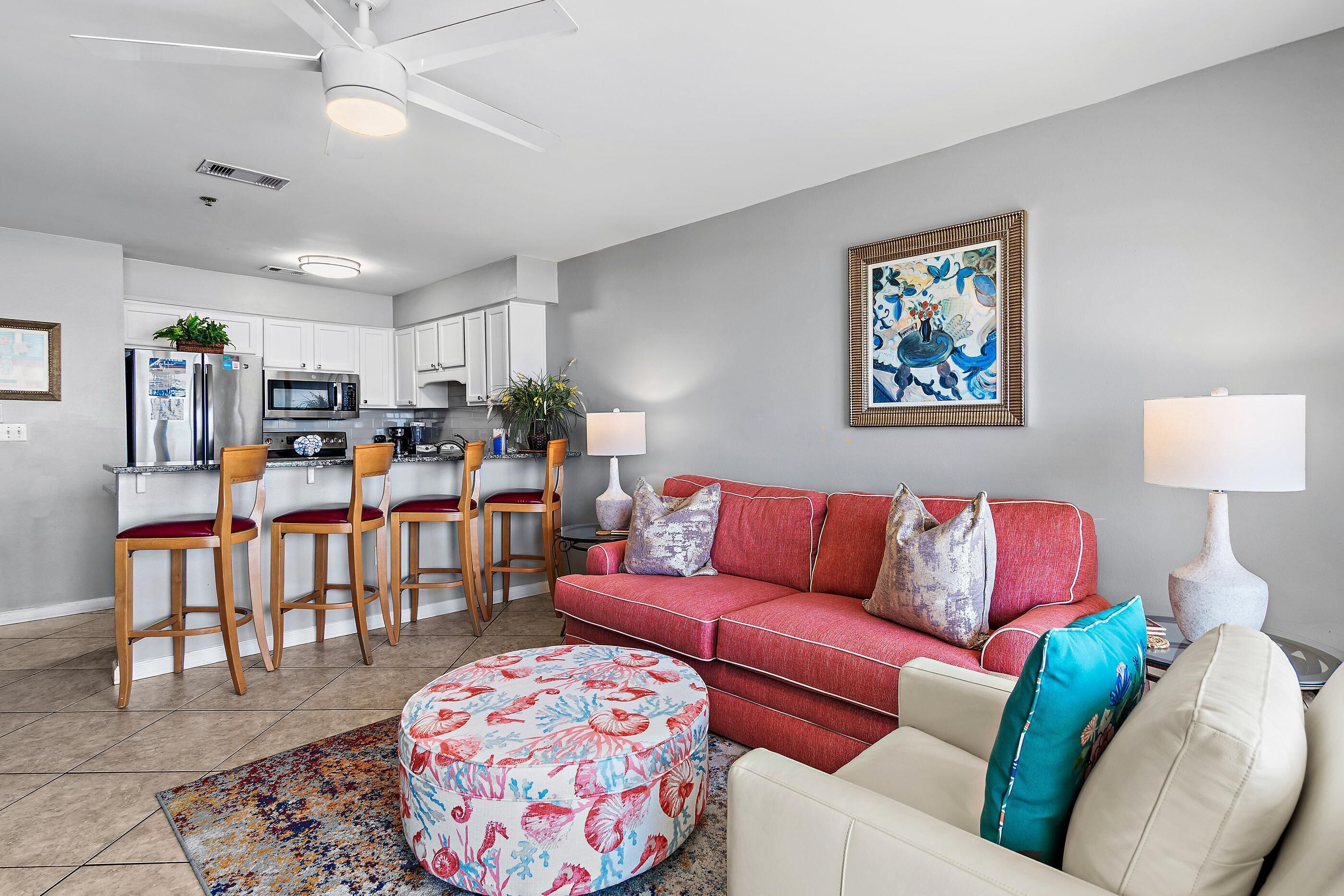 A modern living room with a red sofa, a round ottoman, and a kitchen area with white cabinets and a microwave.