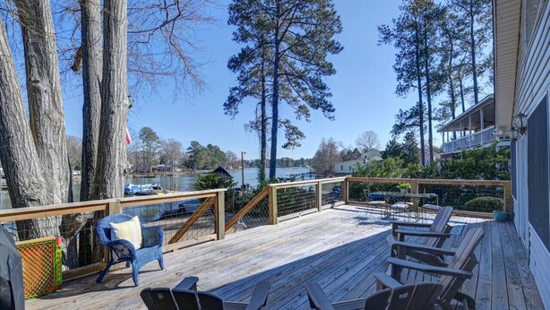 A wooden deck with outdoor seating, overlooking a body of water and surrounded by trees. - Lure & Leisure Lakehouse | Lake Murray 3BR 2BA (Prosperity)
