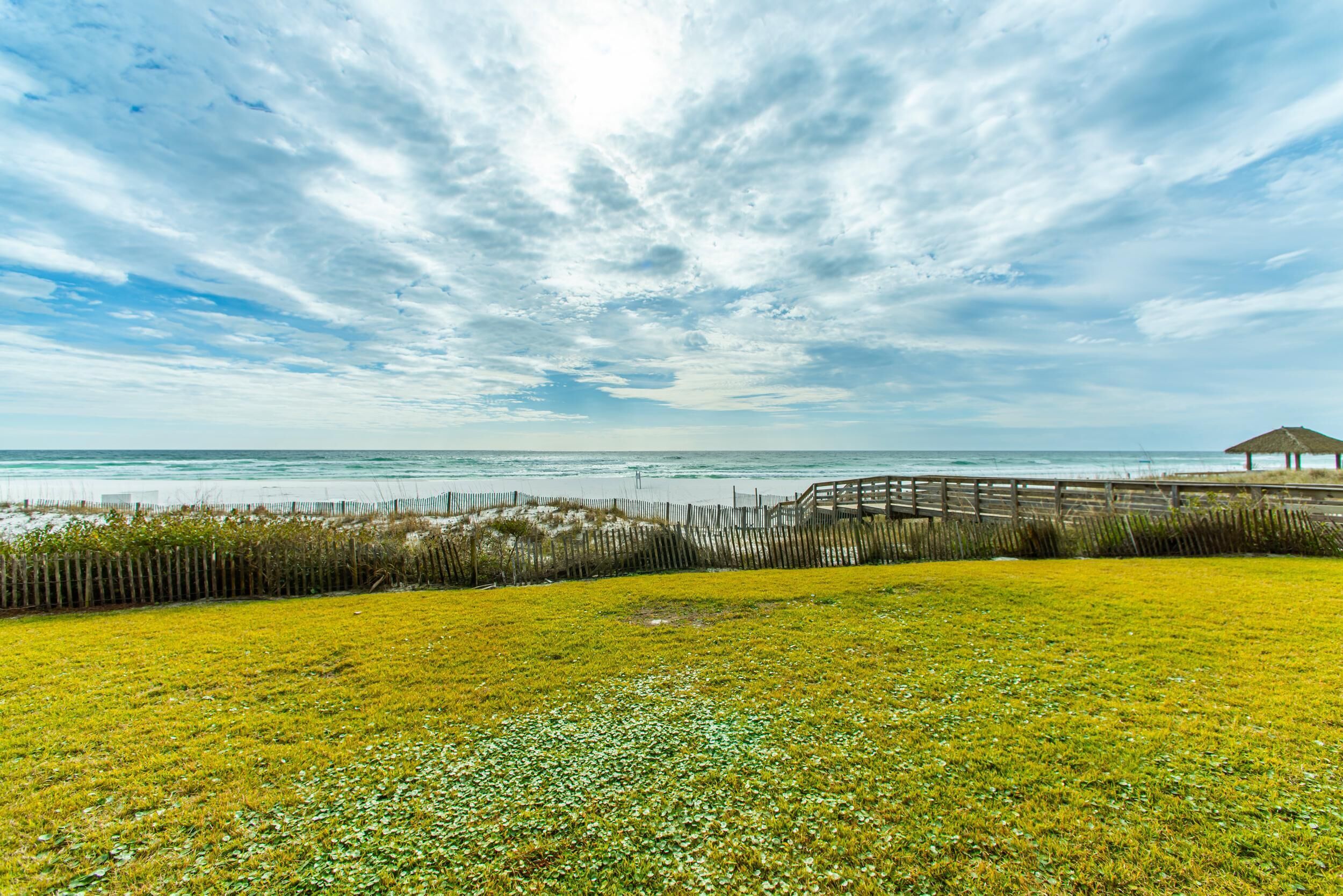 A coastal landscape with a wooden boardwalk, grassy areas, and a beach.