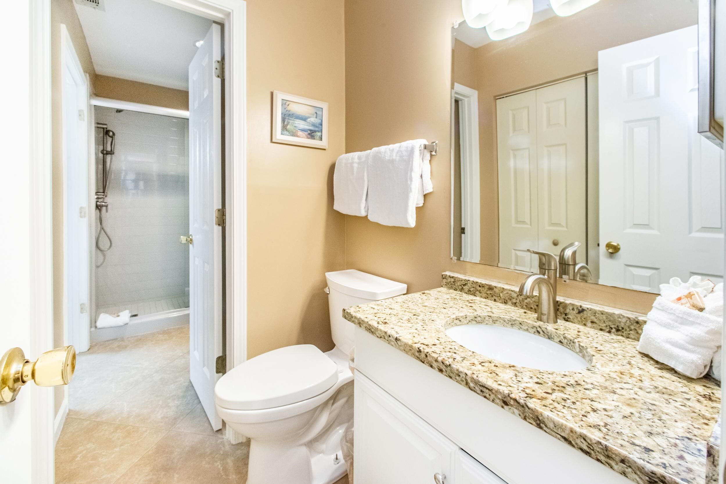 Un baño con inodoro blanco, un lavabo con encimera de granito, una ducha y un perchero para toallas.