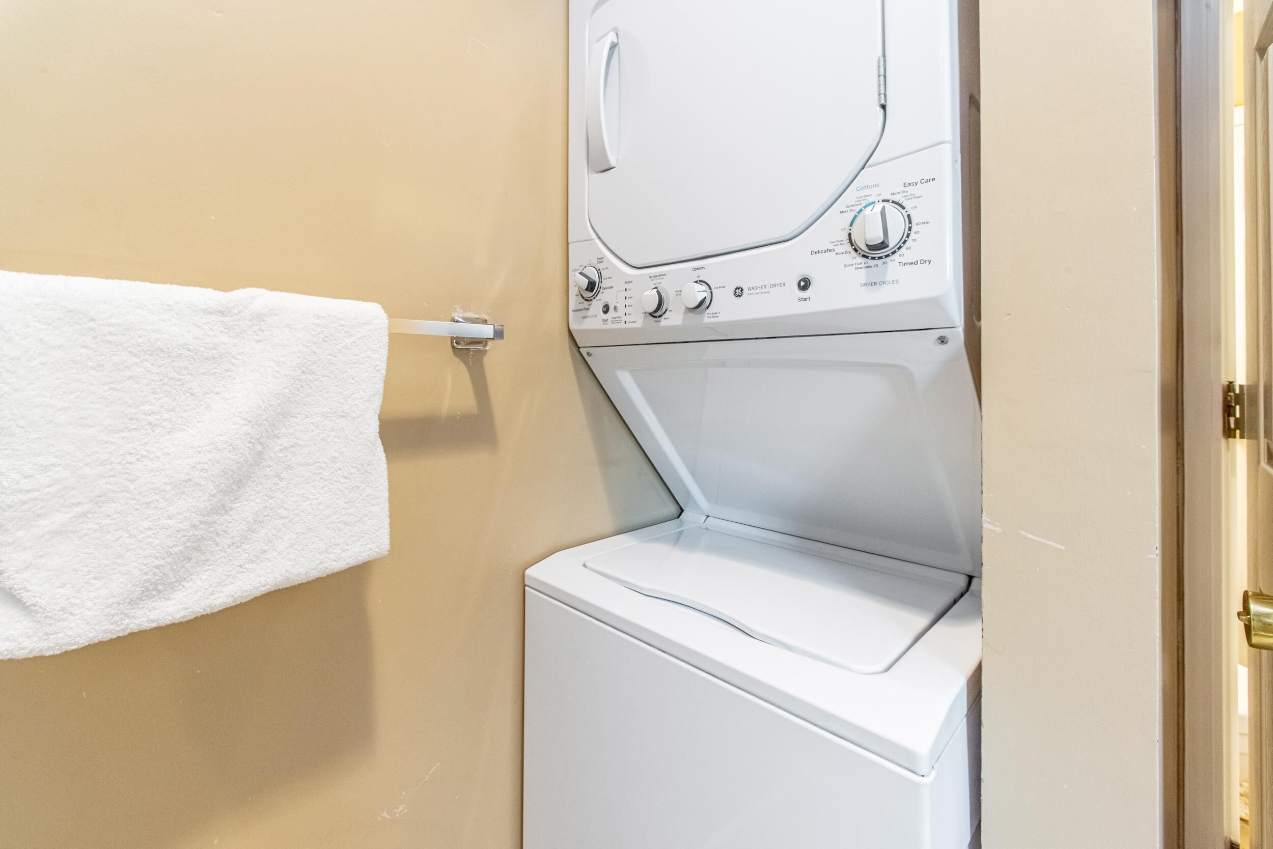 A laundry area with a washing machine and dryer, a towel hanging on a rack, and a door to the right.