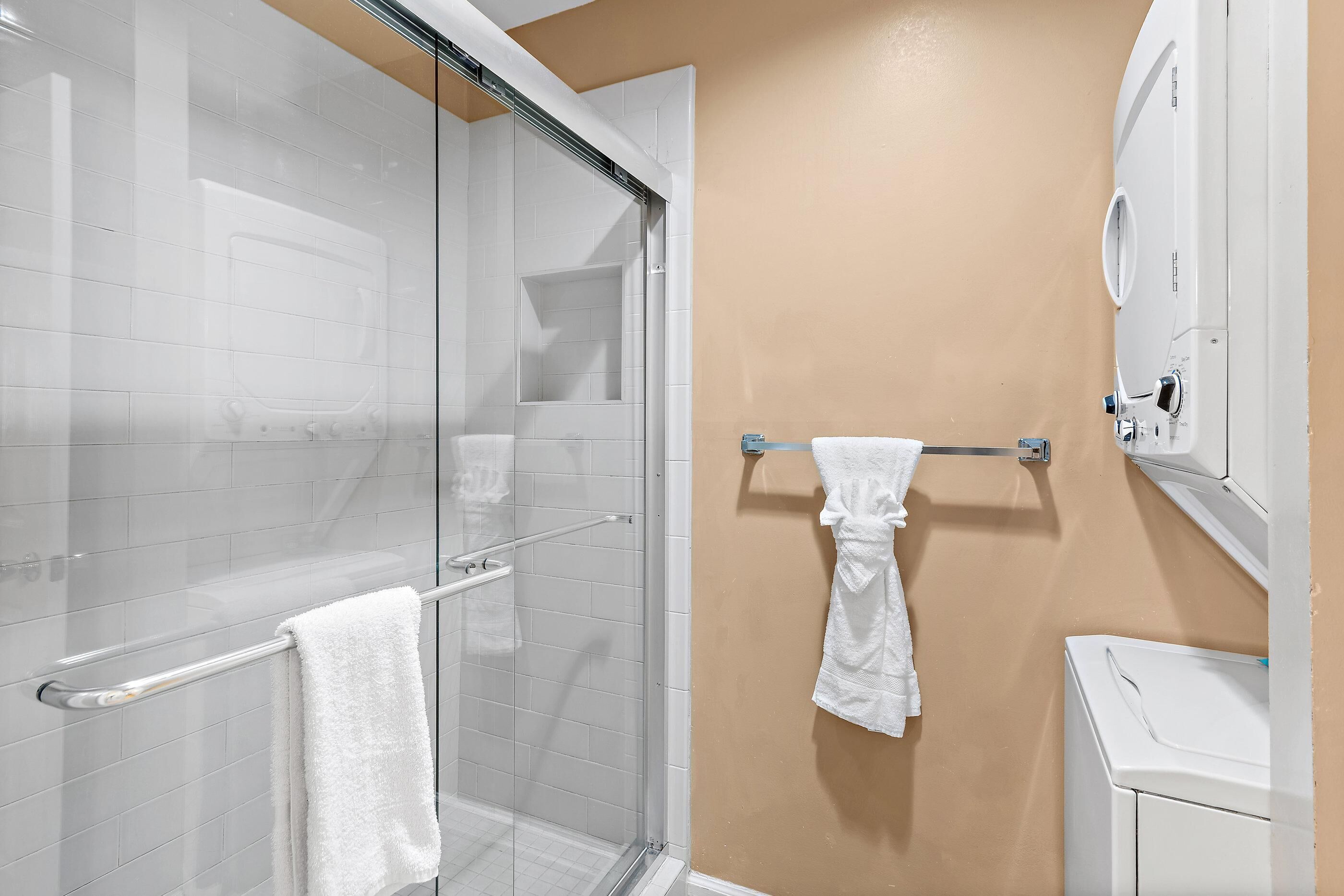 Baño con cabina de ducha de vidrio, toallero y lavamanos blanco.
