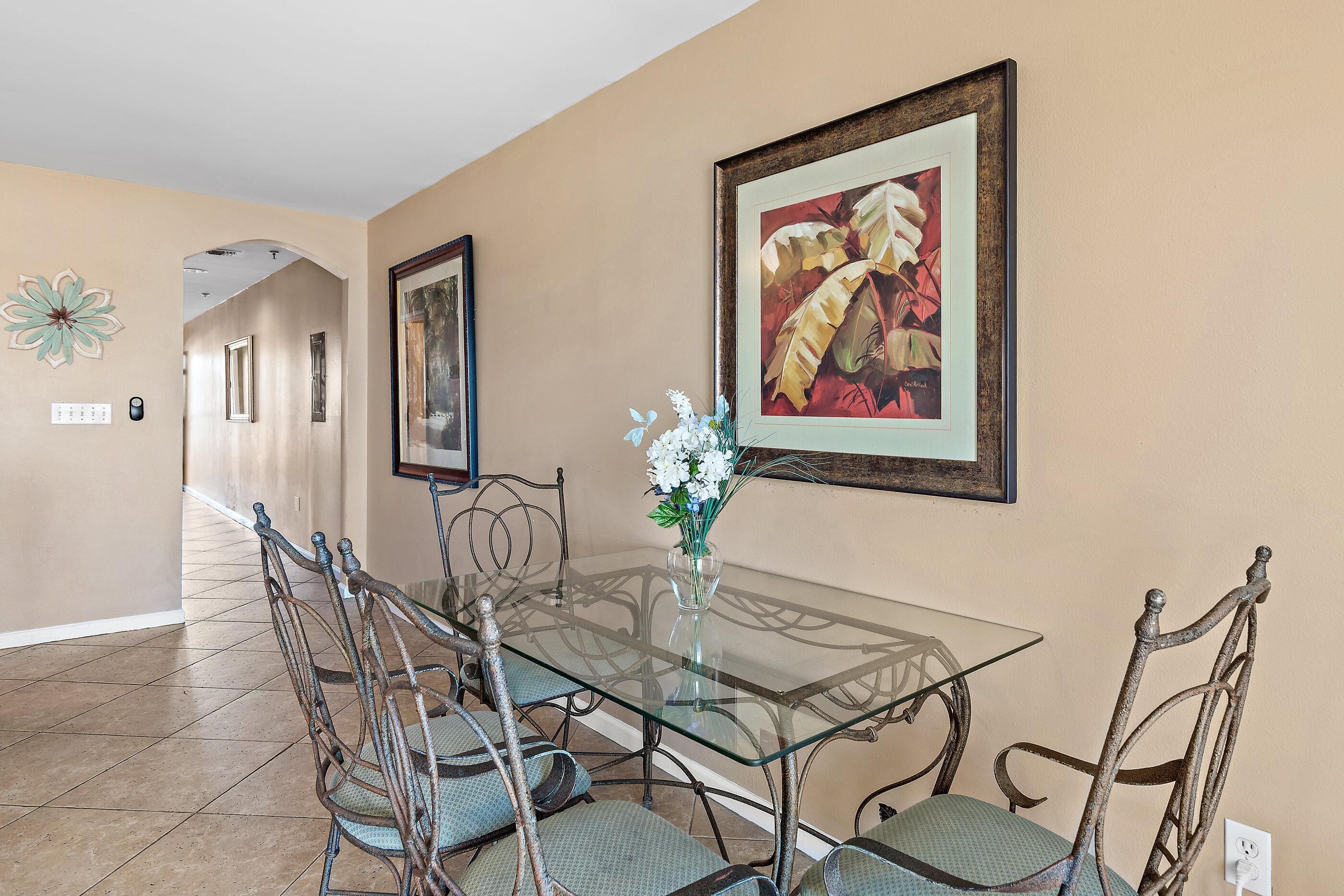 A dining area with a glass table, metal chairs, a vase with flowers, and framed artwork on the walls.