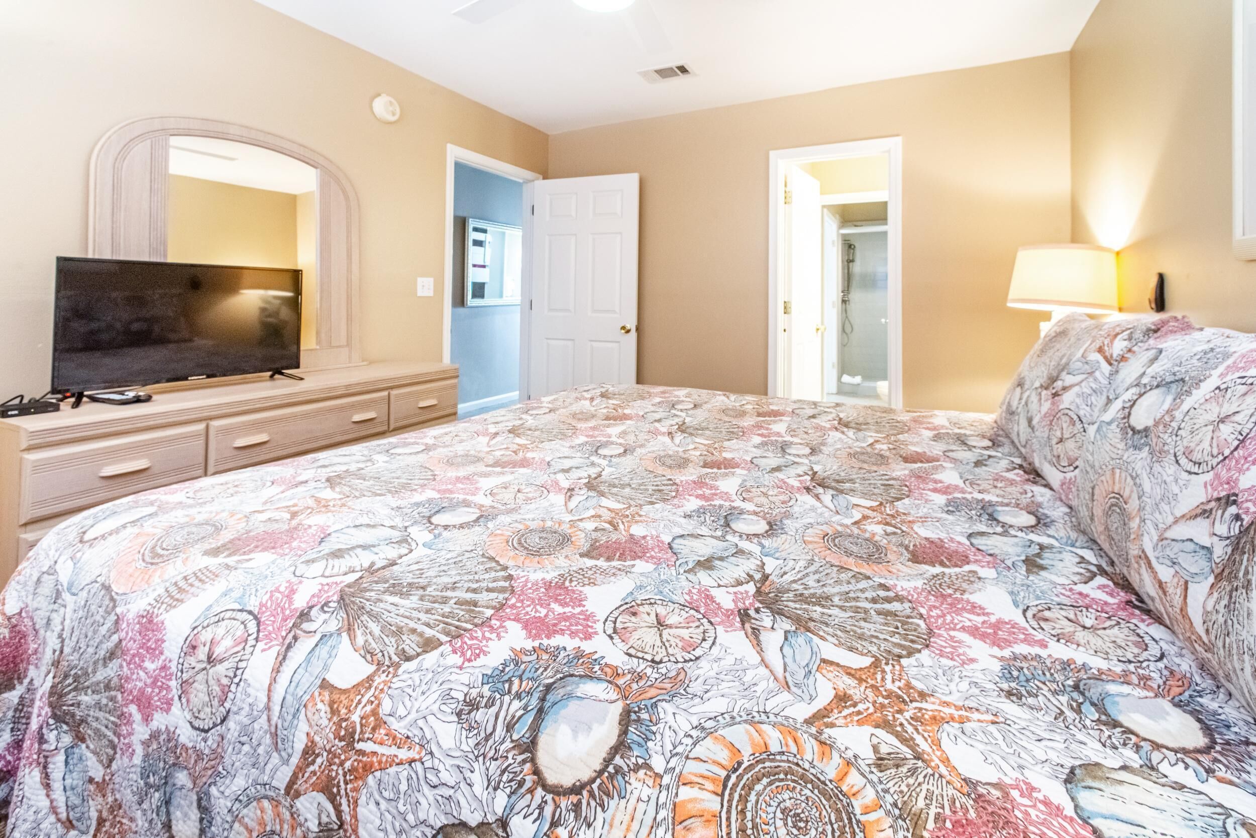 A bedroom with a large bed, a television, a dresser, and a door leading to a bathroom.