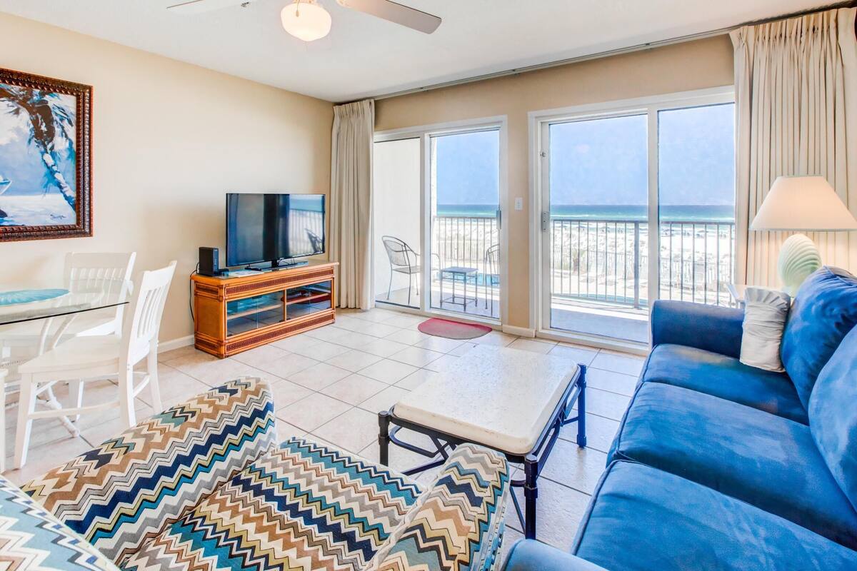 Un salon spacieux avec une grande télévision, un canapé et un balcon offrant une vue sur la plage.