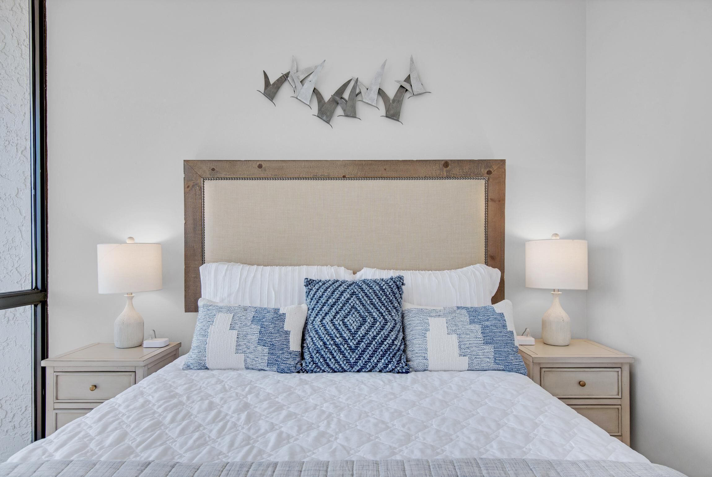 Un lit bien fait, recouvert d’une courtepointe blanche, deux tables de chevet avec des lampes et une œuvre d’art accrochée au mur au-dessus du lit.