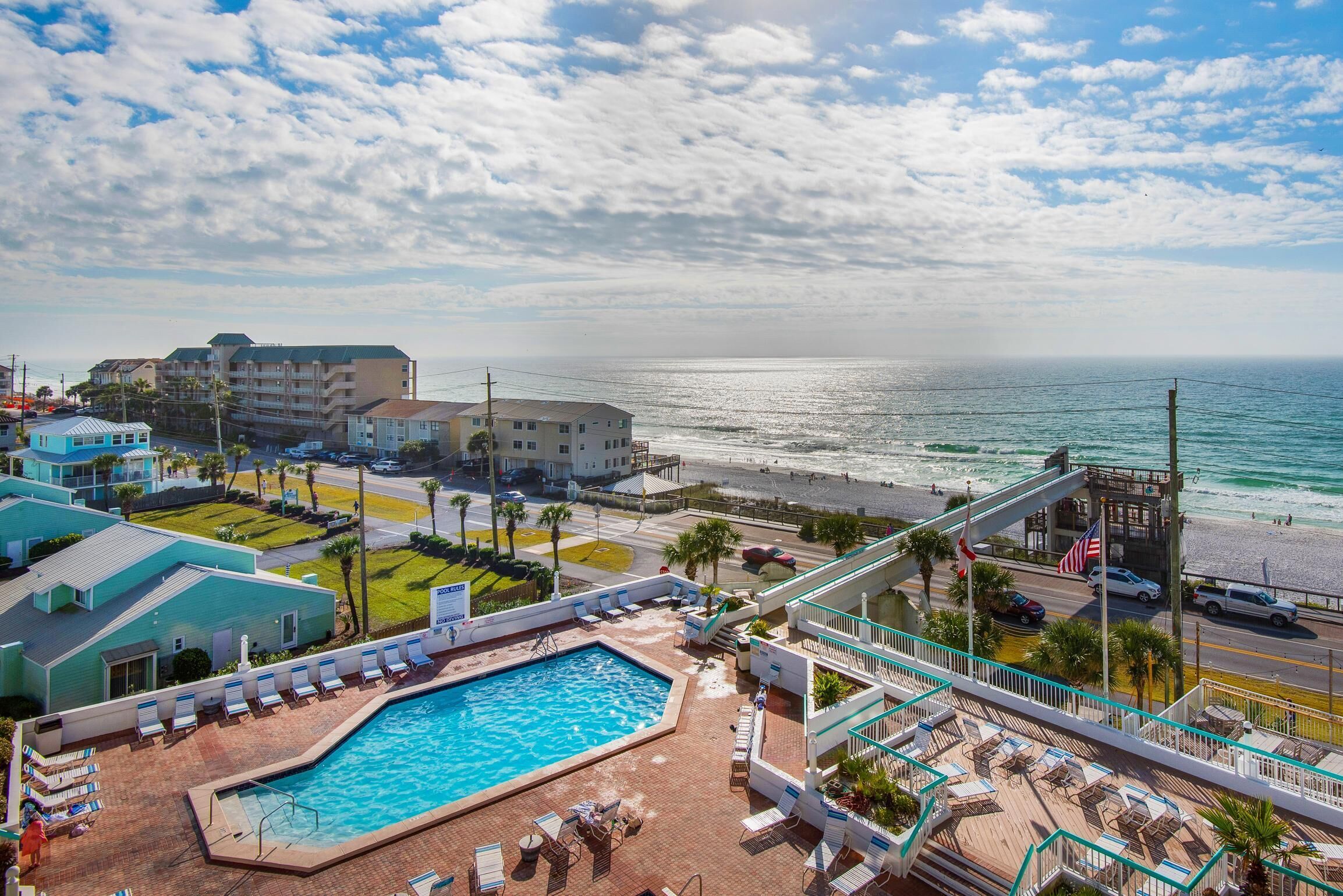 A hotel with a pool, beach view, and a pedestrian bridge.