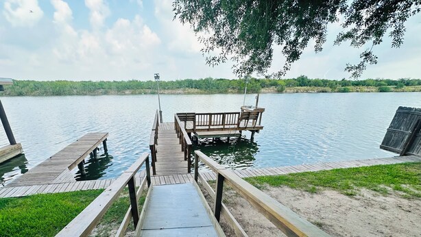 A wooden dock leading to a boat launch area with a grassy bank and a view of a calm lake. - Marina’s Cozy Cottage. Family friendly with cold AC in summer and warm winters! (Rio Hondo)