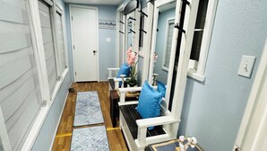 A narrow hallway with wooden flooring, a blue patterned rug, a white bench with blue cushions, a small table with decorative items, and a mirror on the wall. - Marina’s Cozy Cottage. Family friendly with cold AC in summer and warm winters! (Rio Hondo)