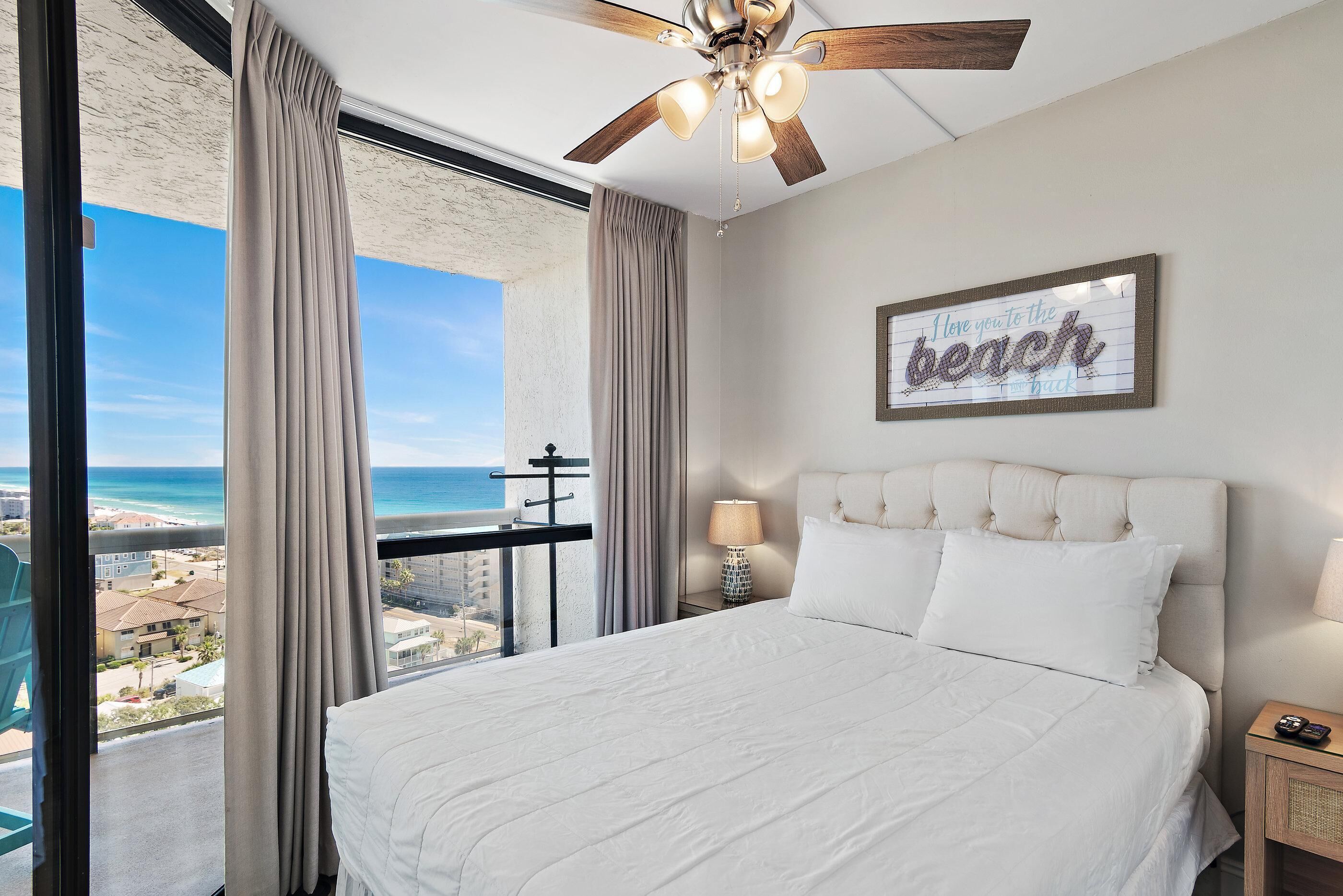 A bedroom with a large bed, a ceiling fan, a view of the beach, and a sign that reads "Here you are to the beach."