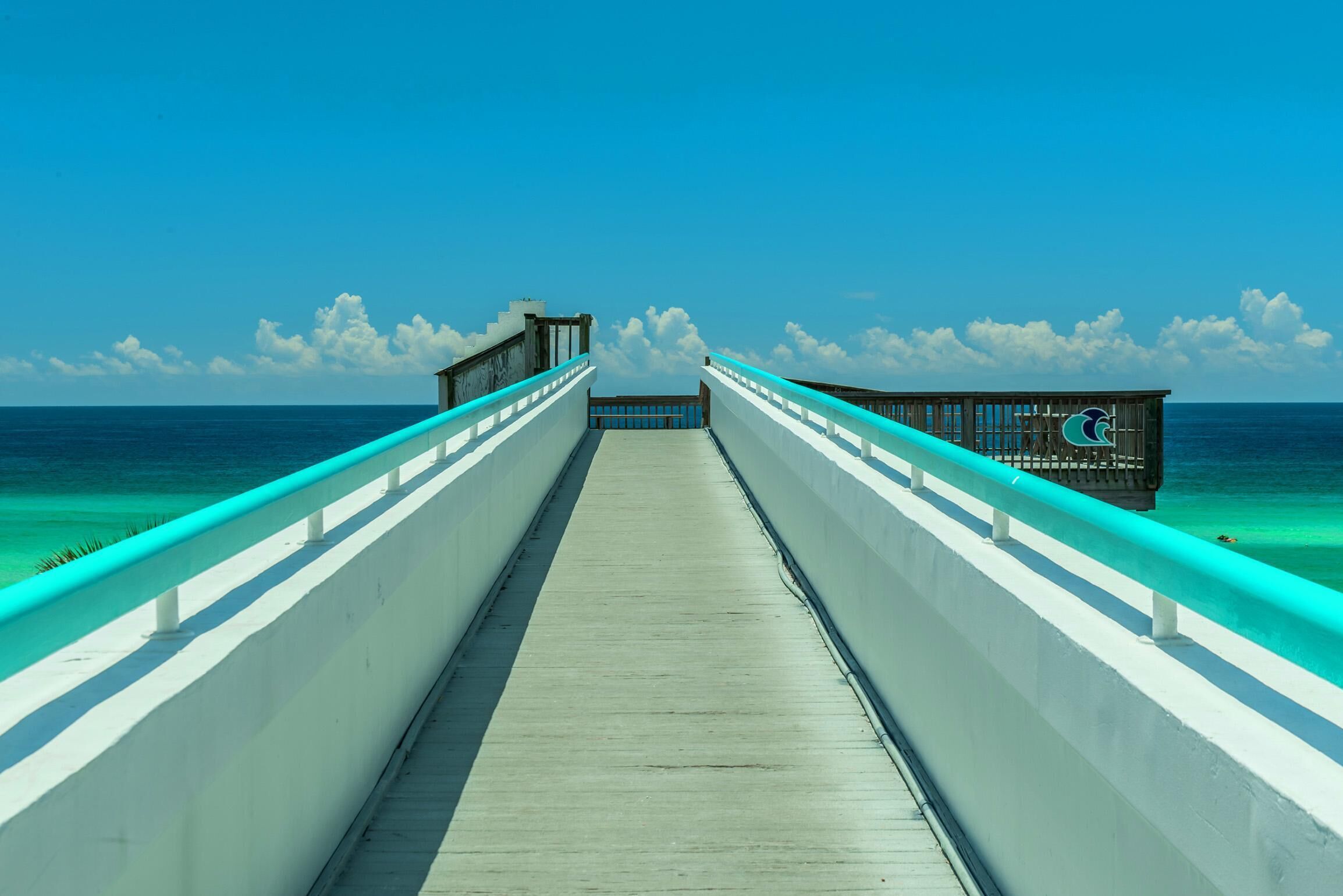 A wooden pier leading to a dock with a clear view of the ocean and a blue sky.