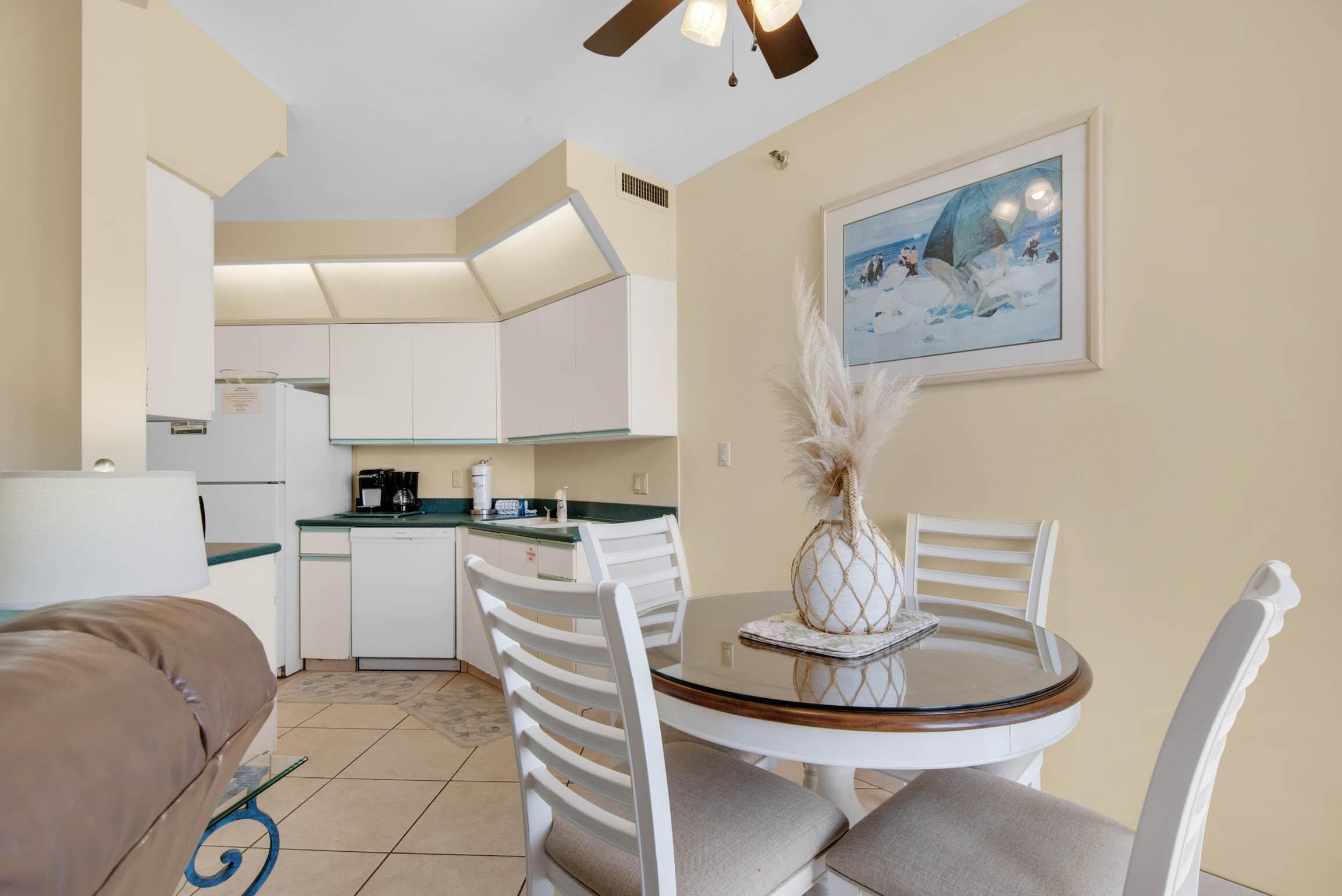 Una cocina compacta con armarios blancos, una mesa de comedor con sillas y un ventilador de techo.