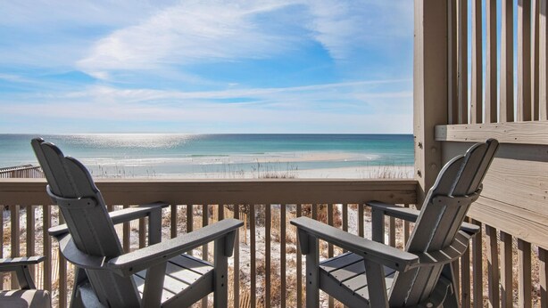Une terrasse en bois avec deux fauteuils Adirondack donnant sur une plage.