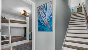 Une chambre avec des lits superposés, un escalier et un tableau représentant un voilier.