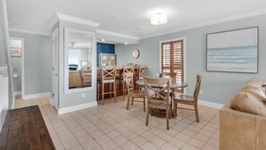 Une cuisine spacieuse avec des meubles en bois, un coin repas doté d’une table ronde et de chaises, et un salon avec un canapé beige.