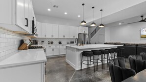 Eine moderne Küche mit weißen Schränken, einer zentralen Kochinsel inklusive Barhocker und einer Treppe, die zu einem Loft führt.