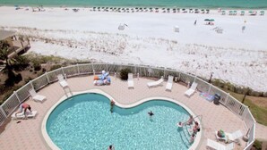 Ein Poolbereich mit Blick auf den Strand, umgeben von Liegestühlen und Sonnenschirmen.