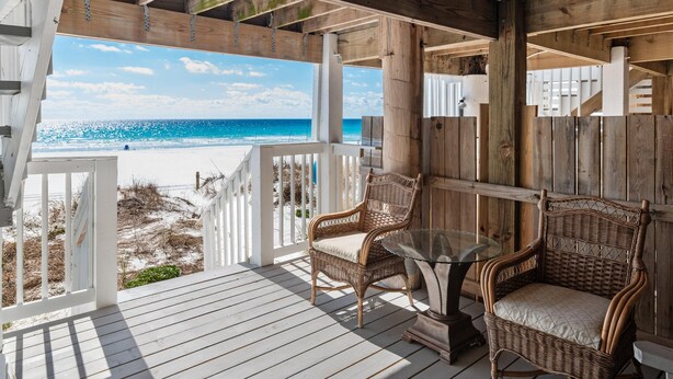 Une terrasse en bois avec des chaises en osier et une table en verre, donnant sur une plage.