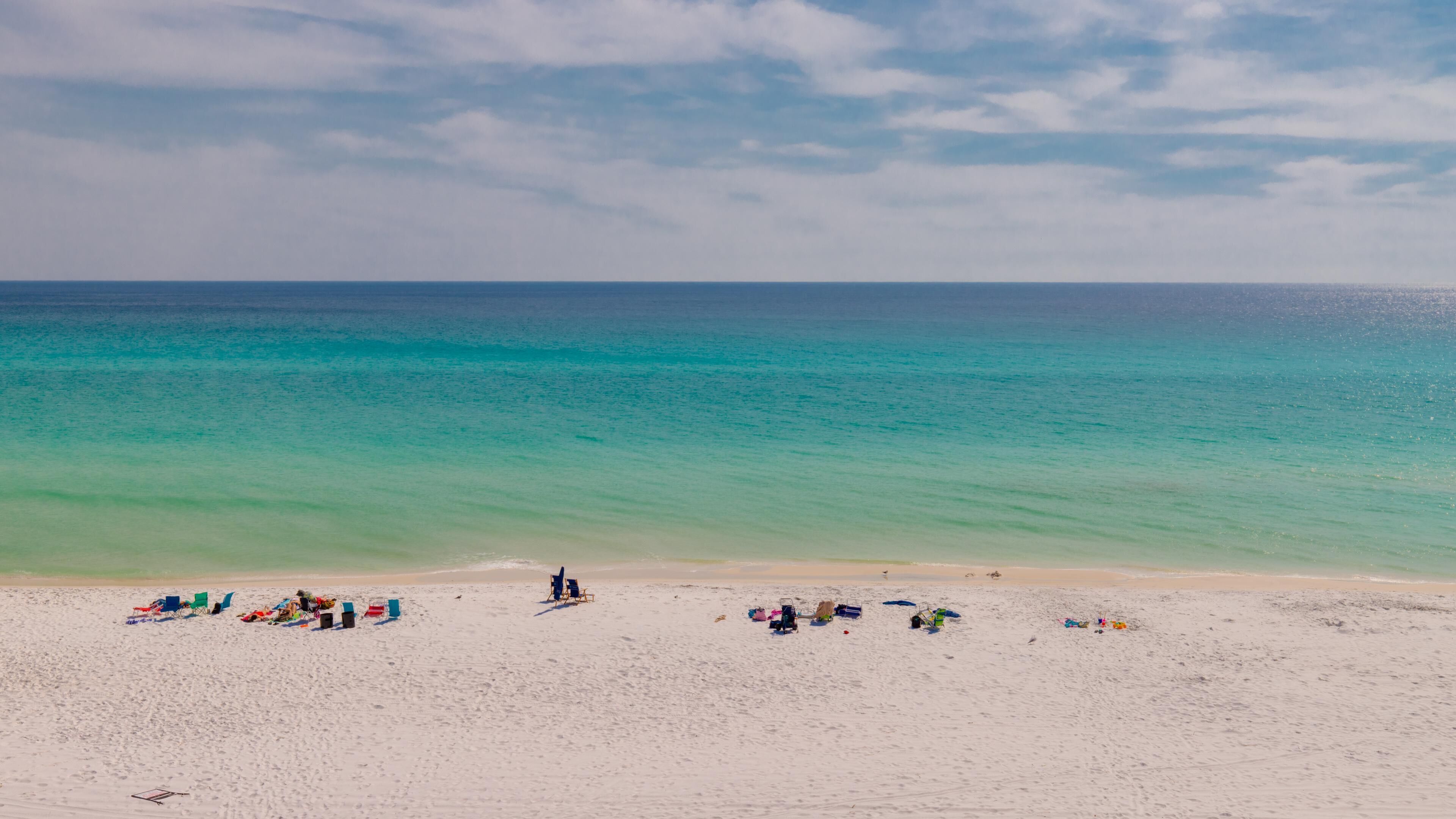 Una playa con arena blanca, un mar azul cristalino y algunas sillas y sombrillas.