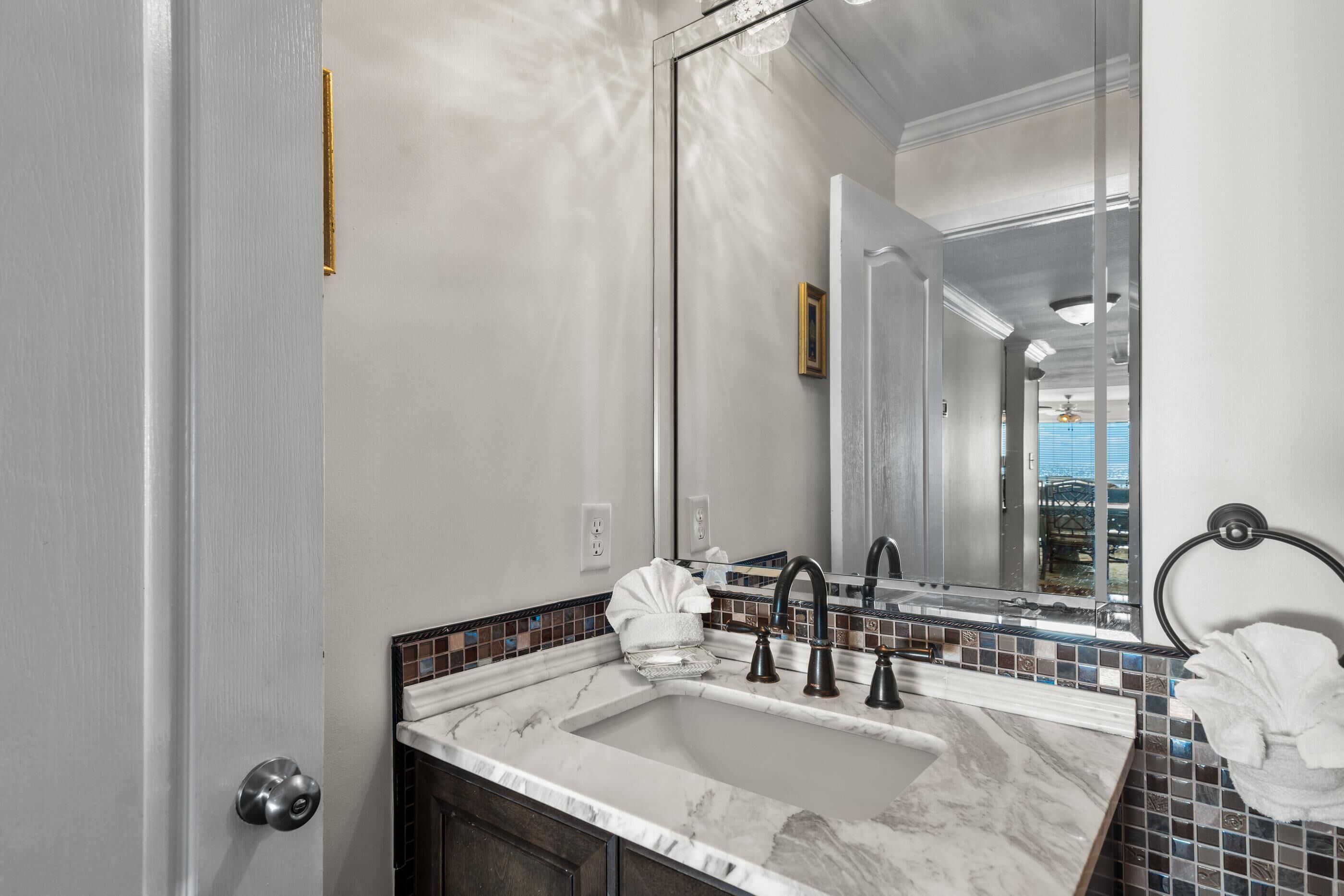A bathroom with a large mirror, a sink with a marble countertop, and a towel rack.