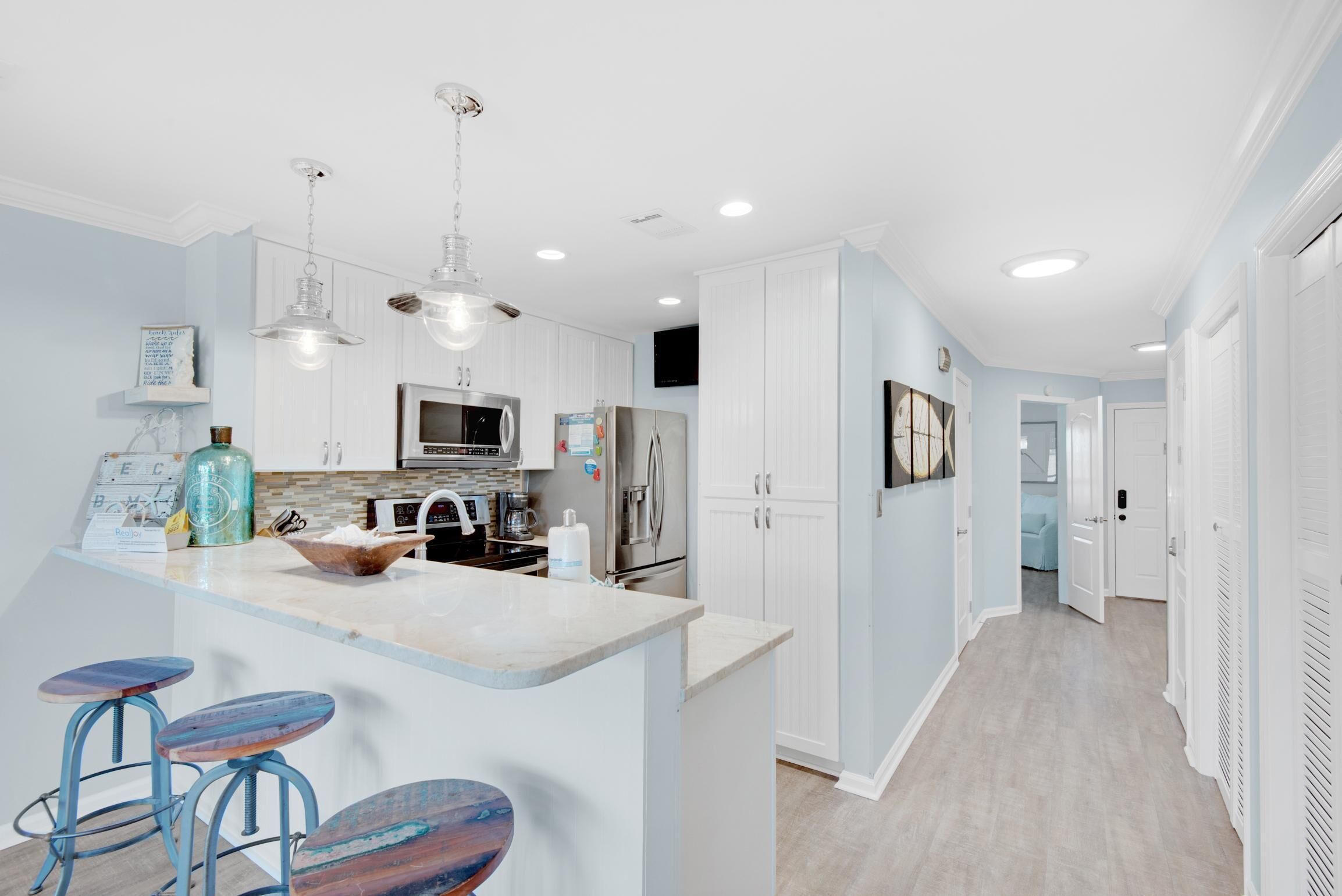 A modern kitchen with white cabinets, a marble countertop, and pendant lighting.