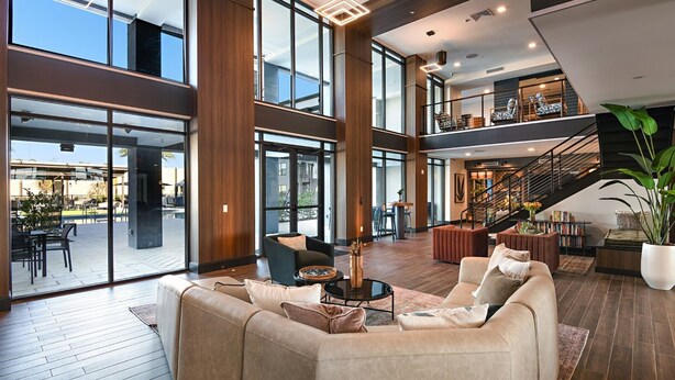 A spacious lobby with a high ceiling, large windows, and a staircase leading to an upper level.