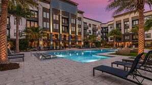 A modern hotel with a swimming pool, lounge chairs, and palm trees.