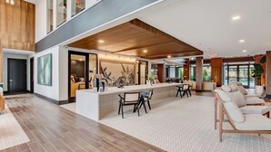 A spacious, modern hotel lobby with a central reception desk, seating area, and large windows offering views of the outdoors.