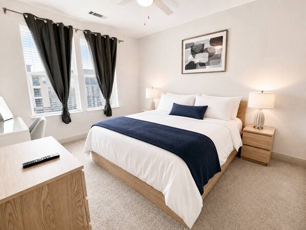 Une chambre d’hôtel avec un lit, des tables de chevet, un bureau et une fenêtre avec des rideaux.