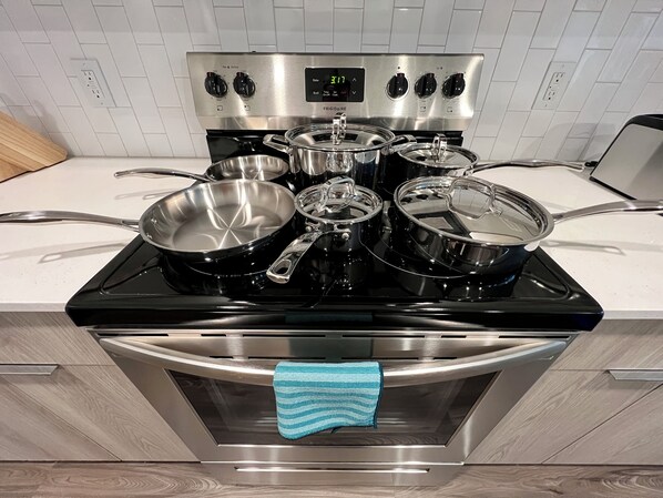 Una cocina con estufa de acero inoxidable, varias ollas y una toalla azul colgada en la puerta del horno.