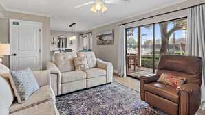 A living room with a beige sofa, a brown leather chair, a ceiling fan, and a large window with a view of the outdoors. - Seascape 38A (Miramar Beach)