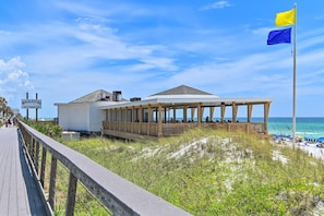 A beachside restaurant with a covered outdoor seating area and a flagpole with a flag. - Memory Maker (Miramar Beach)