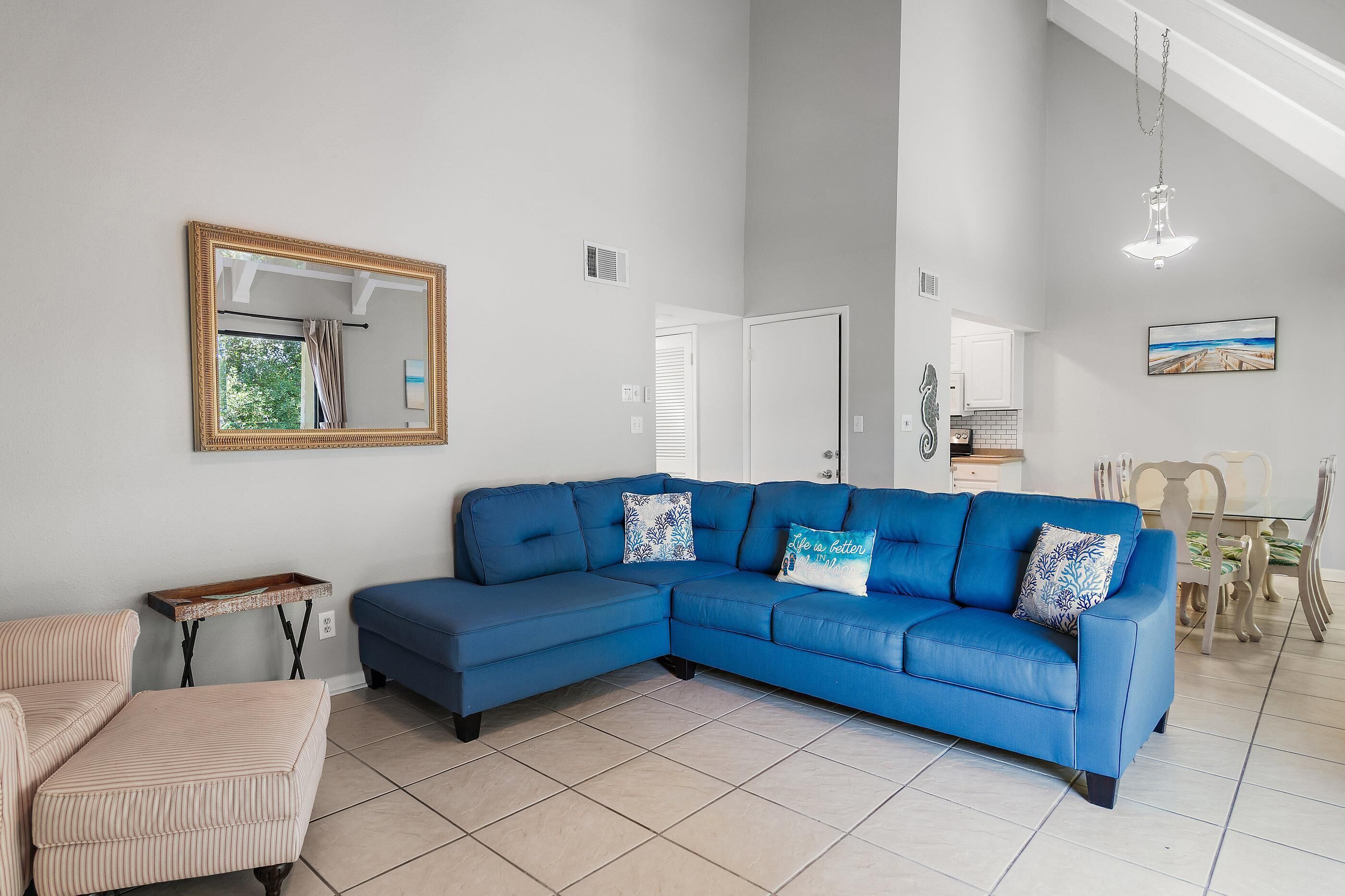 A living room with a blue sectional sofa, a striped armchair, a small wooden table, and a dining area with a glass table and chairs.
