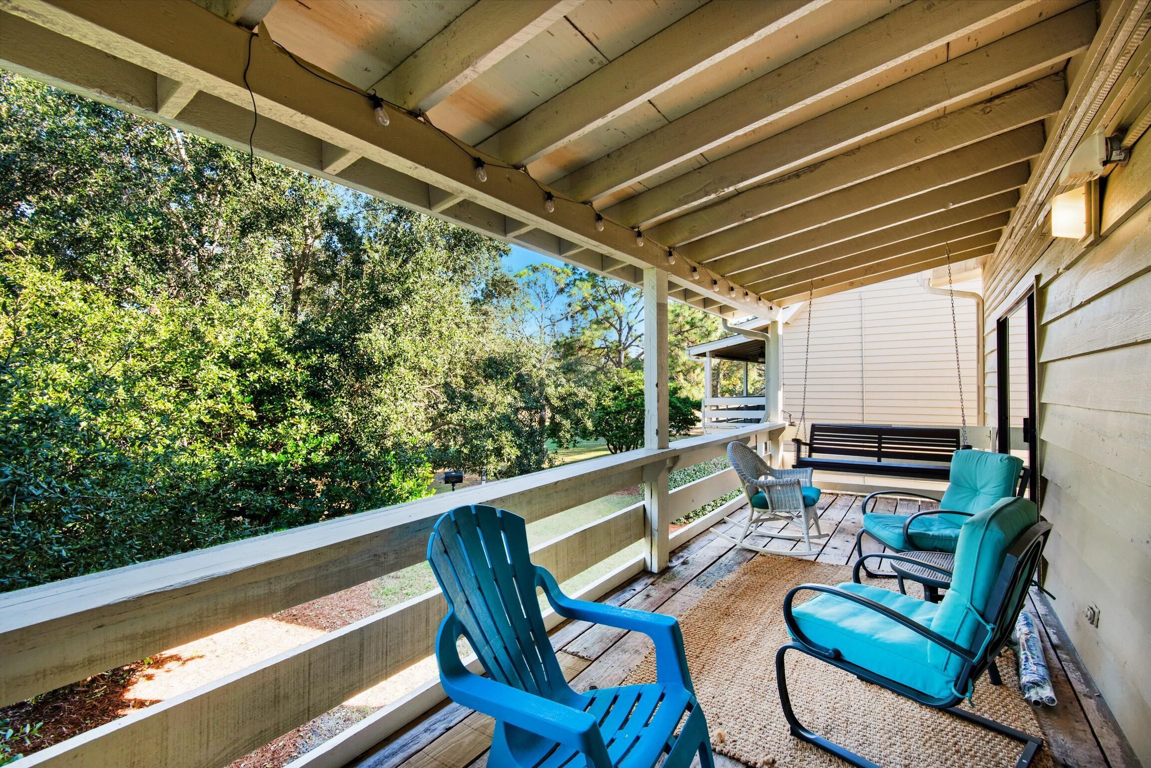 A covered outdoor area with wooden railings, a bench, and two blue chairs.