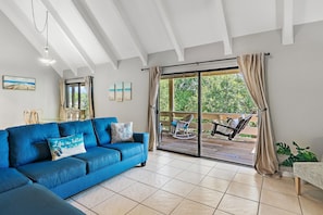 A living room with a blue sofa, a painting of a beach, and a view of a garden through a sliding glass door. - Memory Maker (Miramar Beach)