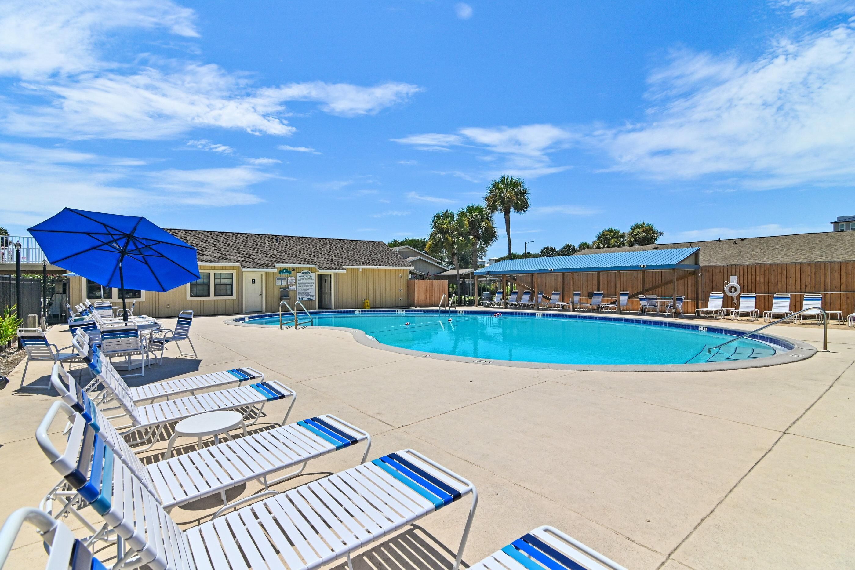 A pool area with lounge chairs and umbrellas, a clear sky, and a building with a sign.
